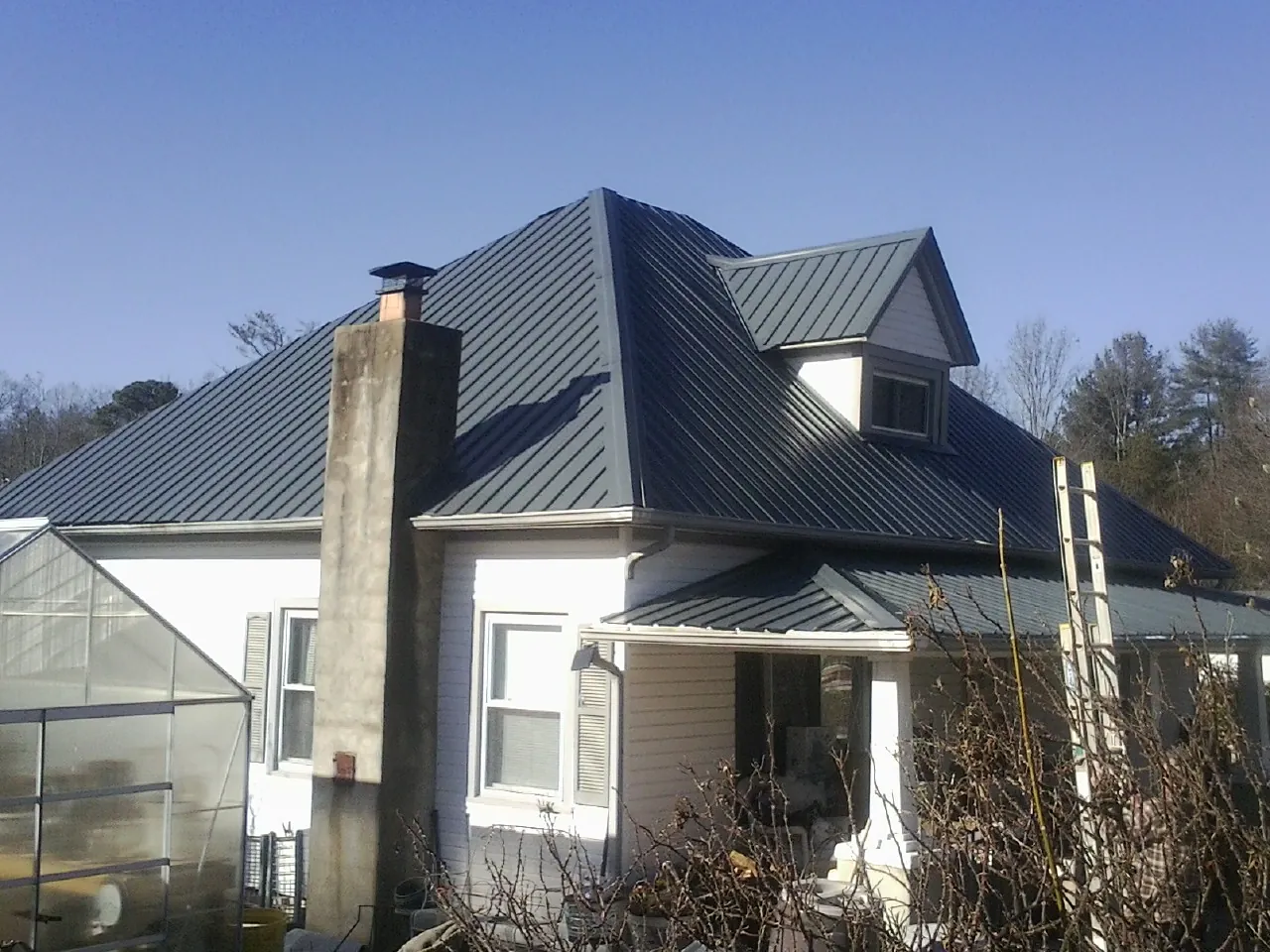 Dark blue standing seam metal roof on a white farmhouse with dormer — Slate & Tile Roof Repair by Roofing Brothers in Albany