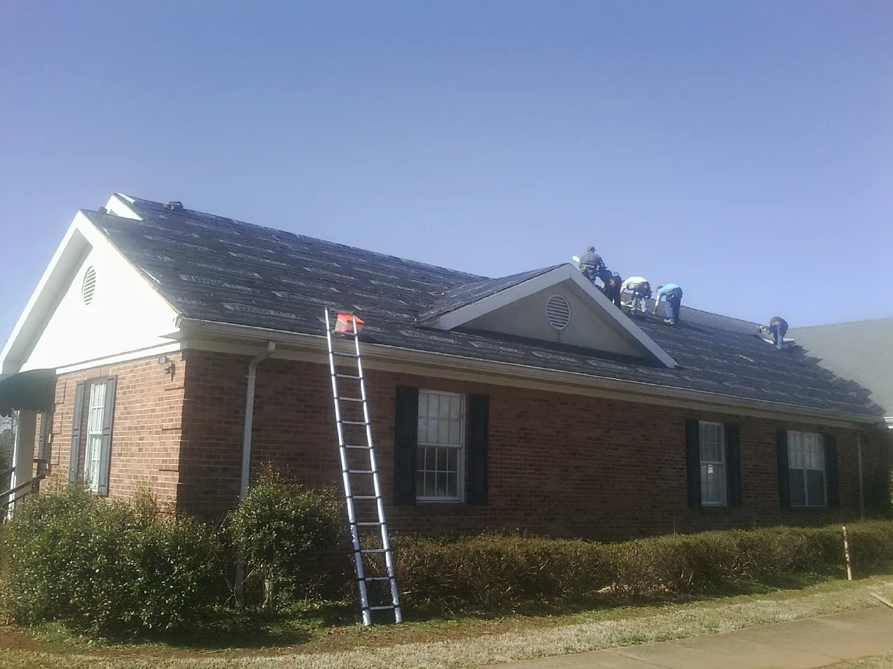 Crew tearing shingles off a brick ranch roof with a ladder set — Metal Roof Repair work by our crew in Albany