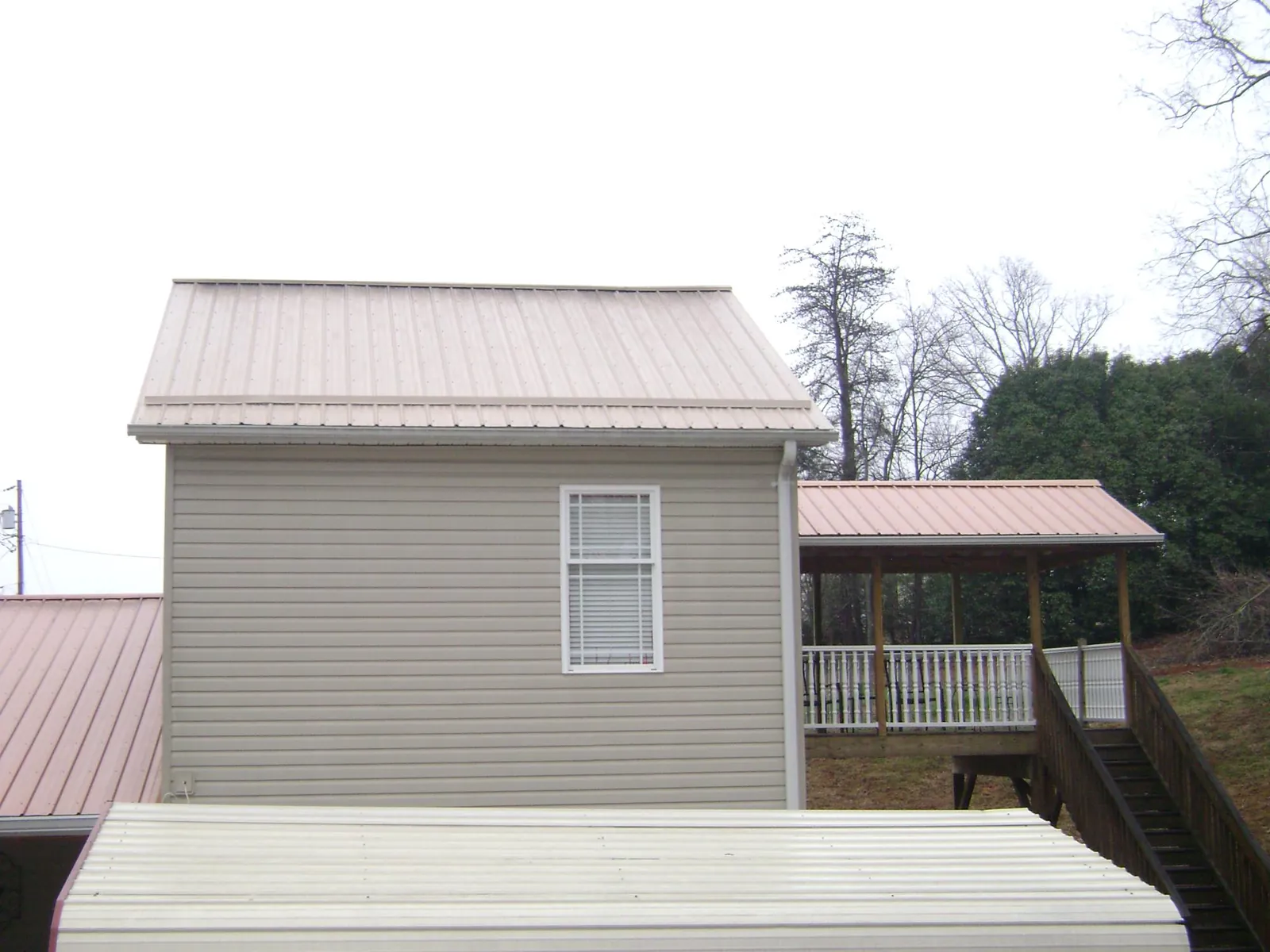 Tan metal roofs on a two story addition and attached porch, from a Roof Replacement job in Albany